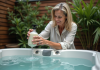 Spa propre : Comment maintenir l’eau propre avec des astuces DIY ! Femme versant une solution de nettoyage dans un spa extérieur