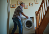 Machine à laver : comment transporter facilement dans les escaliers ? Homme d'âge moyen manœuvrant un lave-linge dans un escalier étroit