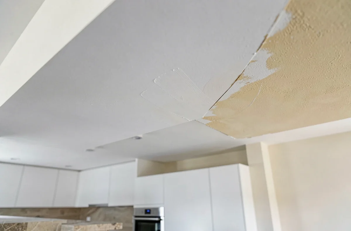 Plafond partiellement réparé montrant le contraste entre la zone rebouchée lisse et l'ancienne surface jaunie